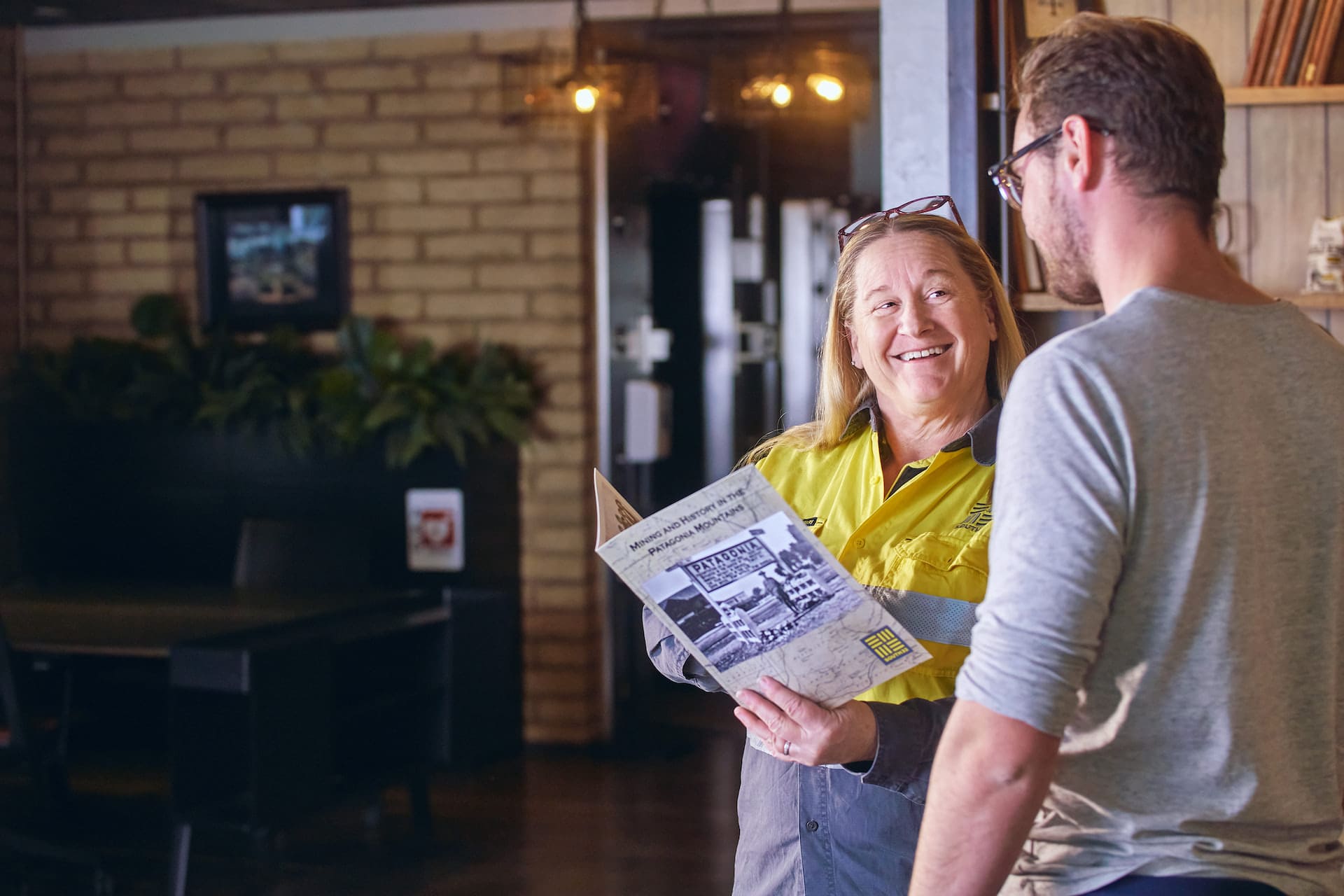 Smiling woman showing a brochure entitled "Mining and history in the Patagonia mountains" to a young man.