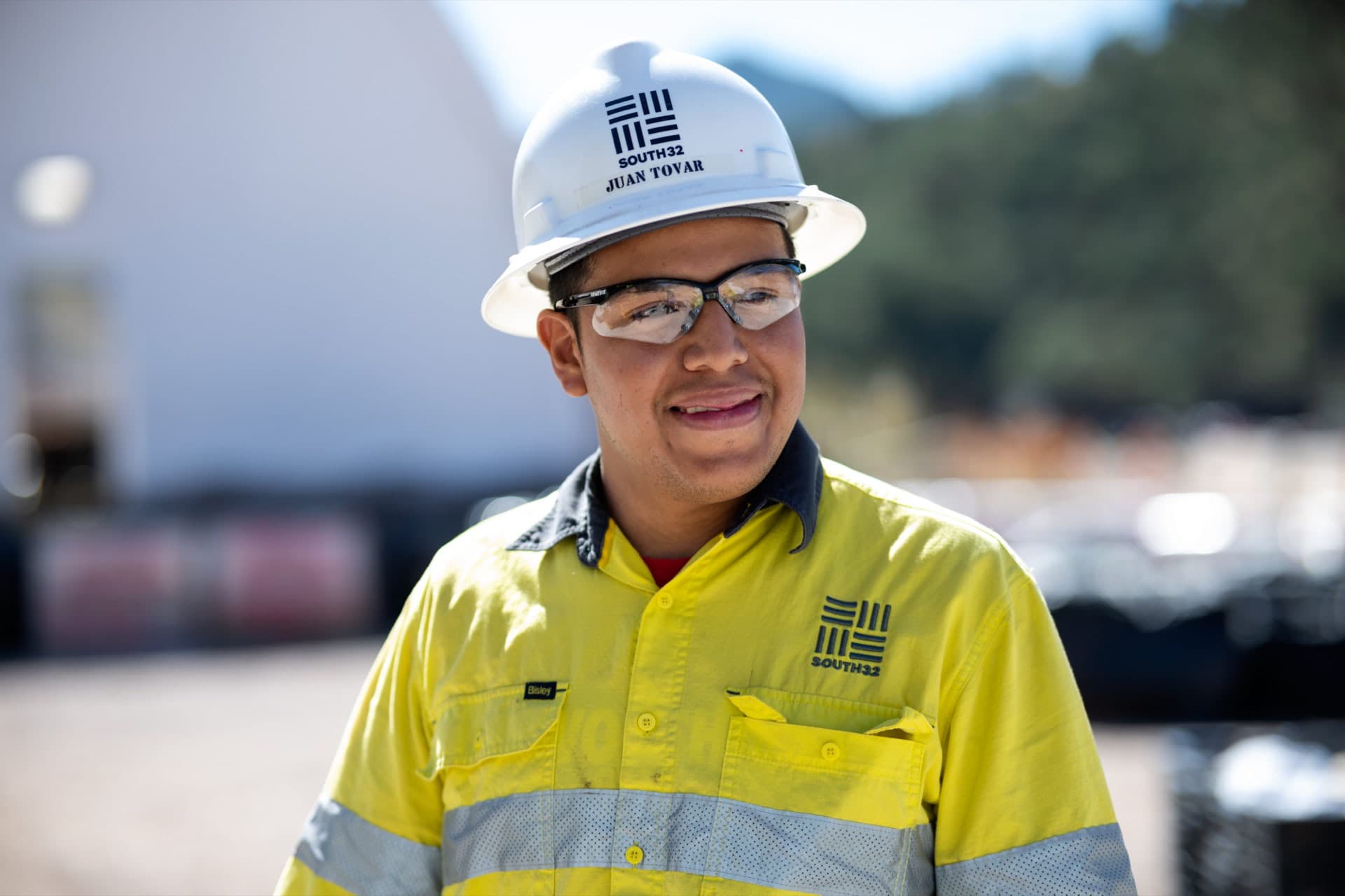 Smiling man in hard hat, safety glasses, and South32 branded workshirt.