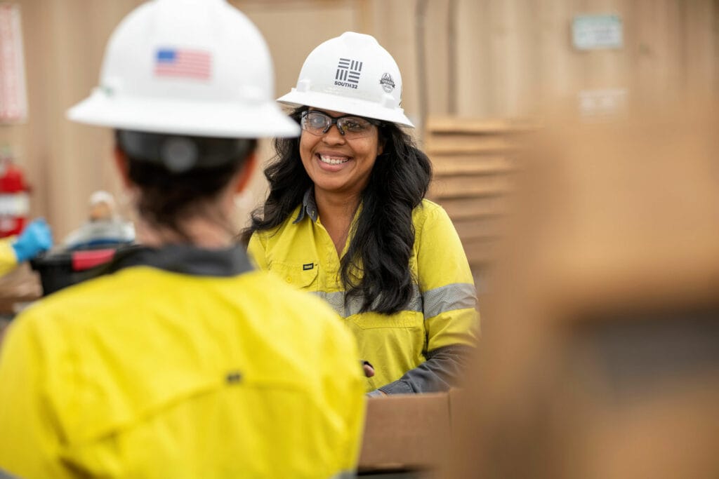 Smiling woman in South32 work shirt and hard hat.